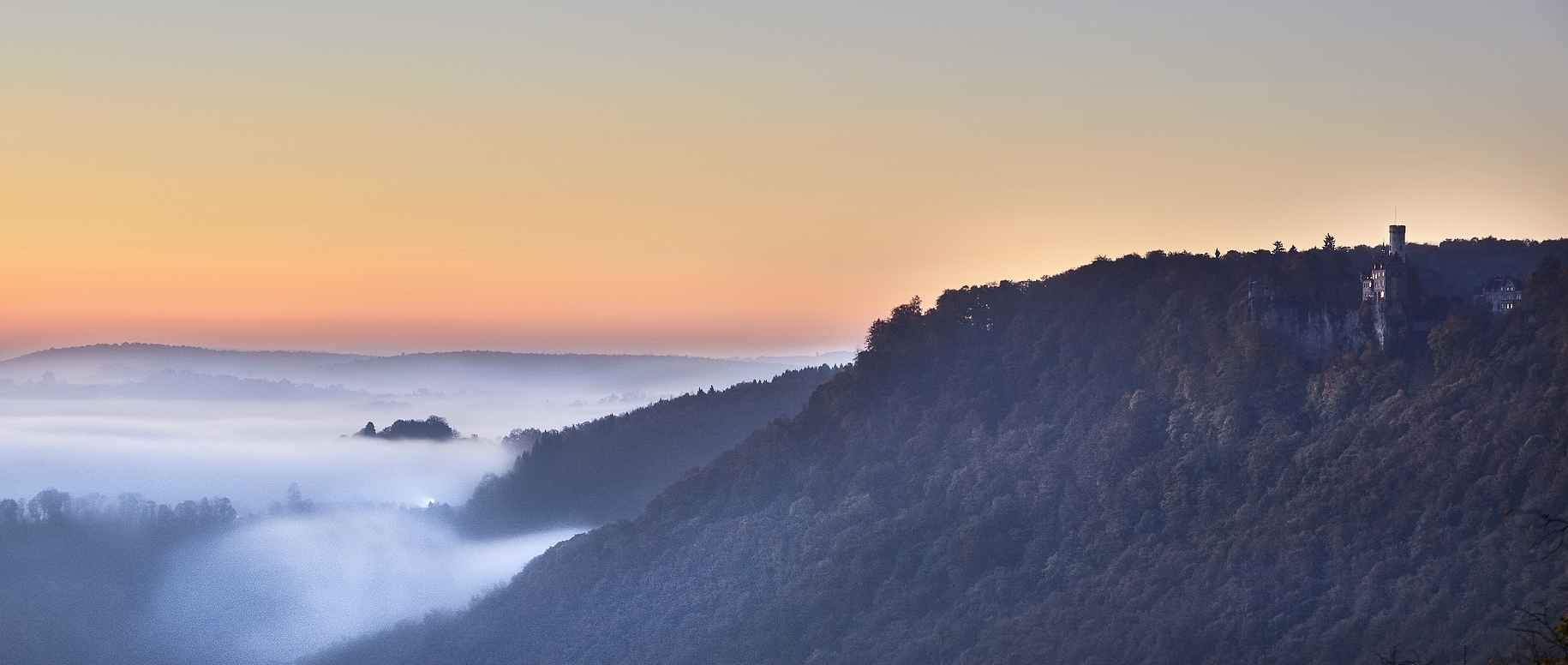 Blick auf die Burg Lichtenstein und Nebelmeer im Tal - der Albtrauf bei Sonnenaufgang.