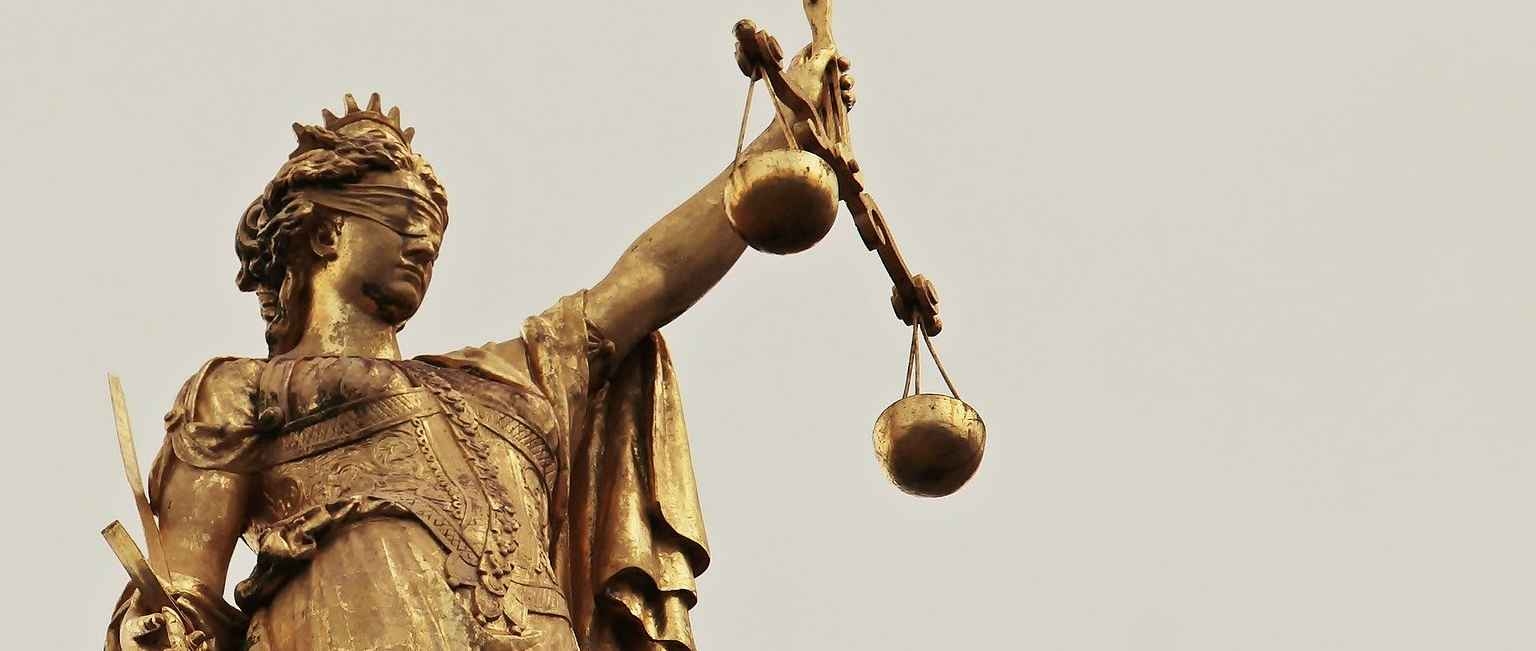 Die Figur Justitia hält in der einen Hand die Waage und in der anderen Hand das Schwert.